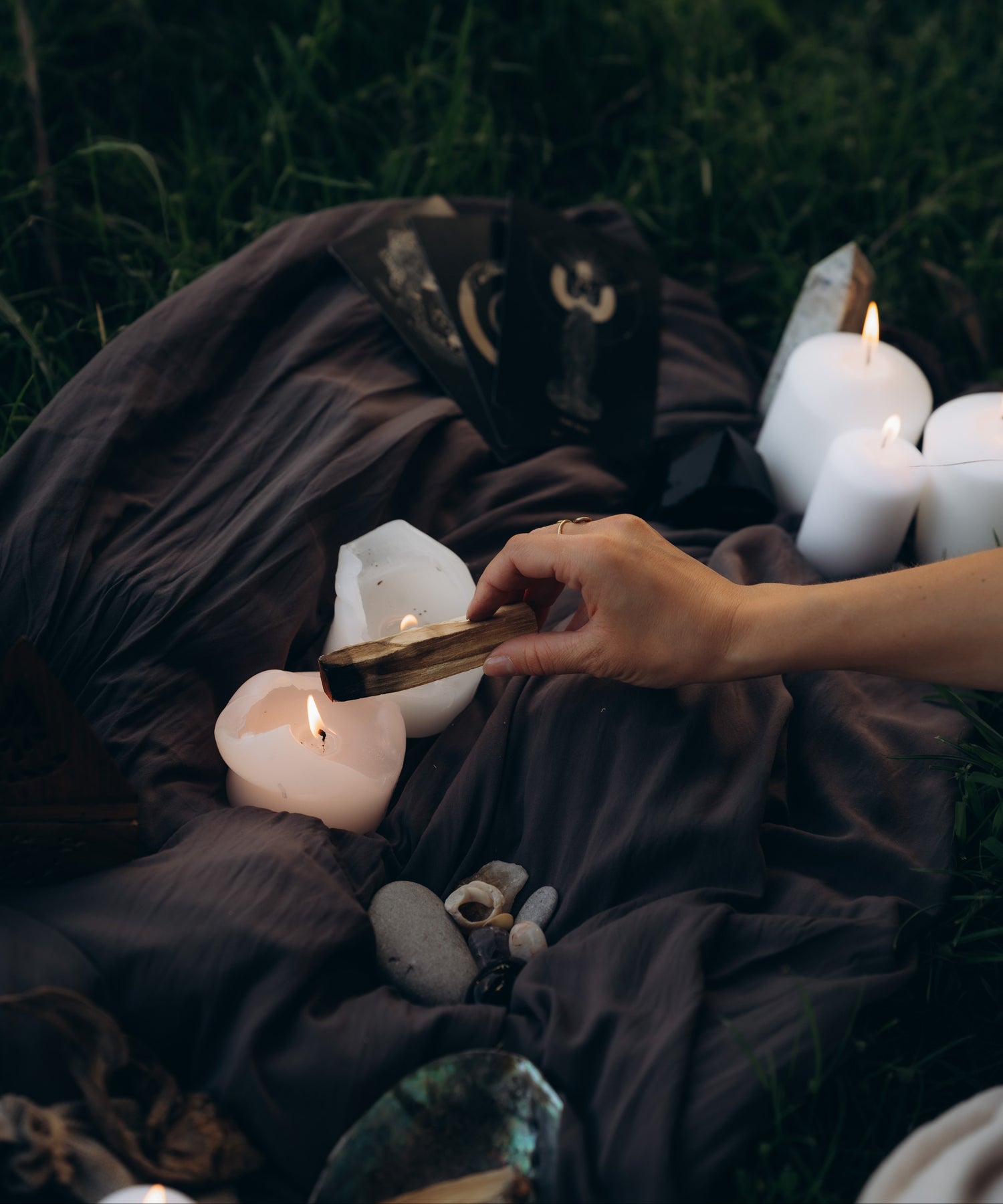 Person holding a palo santo over lit candles on a dark blanket outdoors